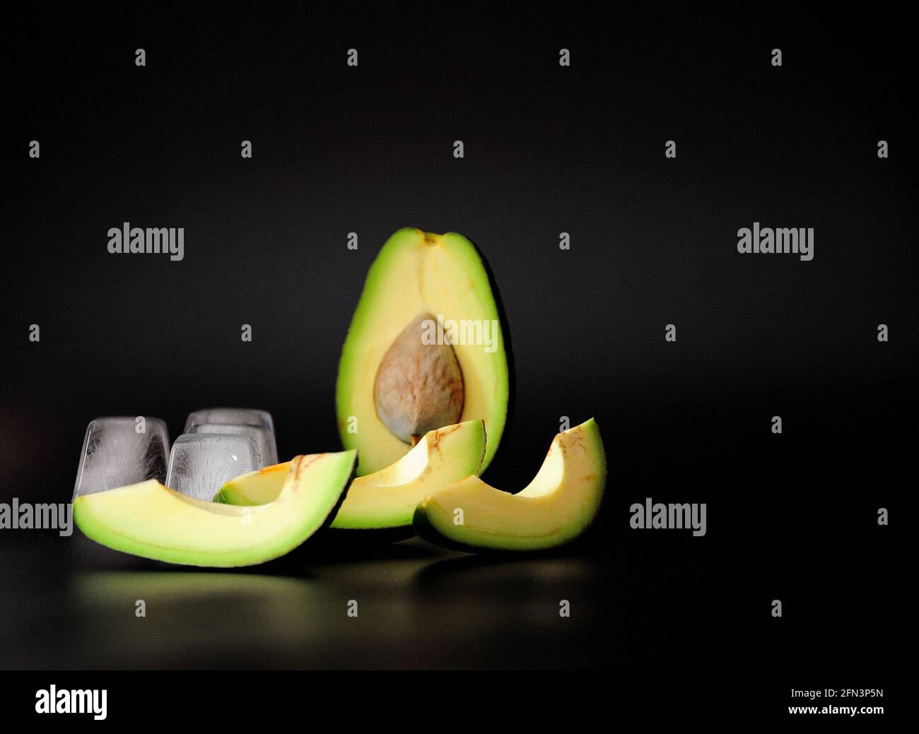 Cut ripe avocado and melted ice cubes on a black background. Close-up ...