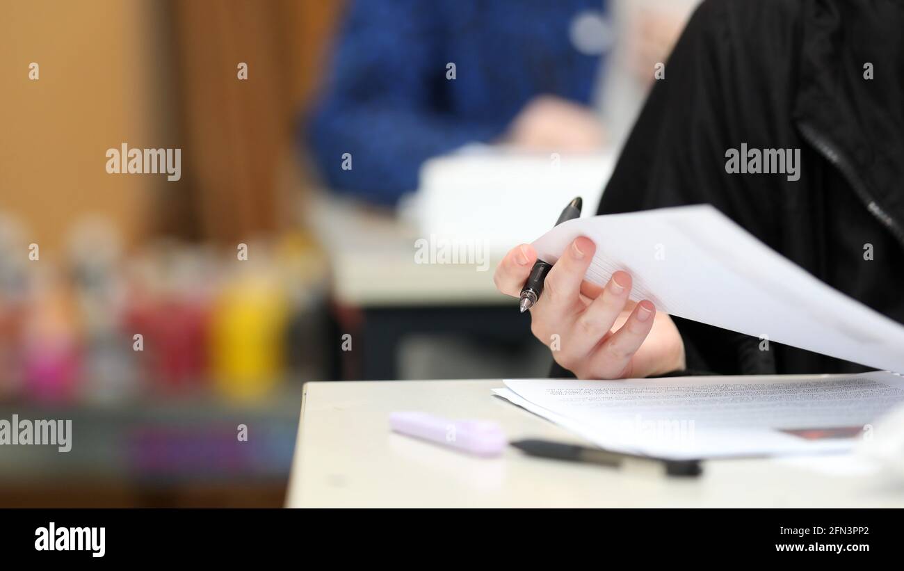 A close up isolated students hand holding a pen checking their answers during class, exam or lesson time at school. Bright colors and second student b Stock Photo