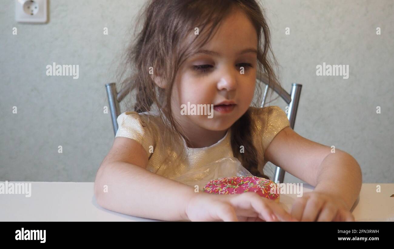 Little happy cute girl is eating donut. child is having fun with donut. Tasty food for kids. Funny time at home with sweet food. Bright kid. Donut wit Stock Photo