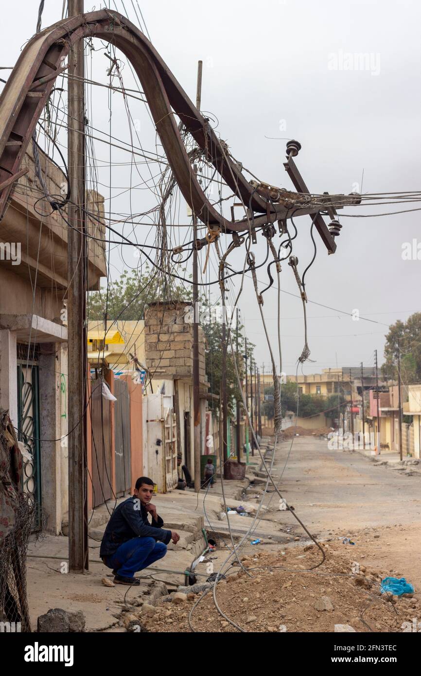 A man crouches under a destroyed utility pole during the early days of the Mosul Operation in Al Bakir district of East Mosul, Iraq. Stock Photo