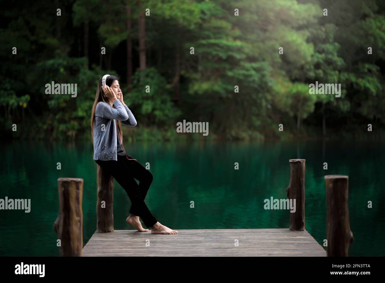 Beautiful young woman with headphones relaxing on the dock, she is listening to music Stock Photo