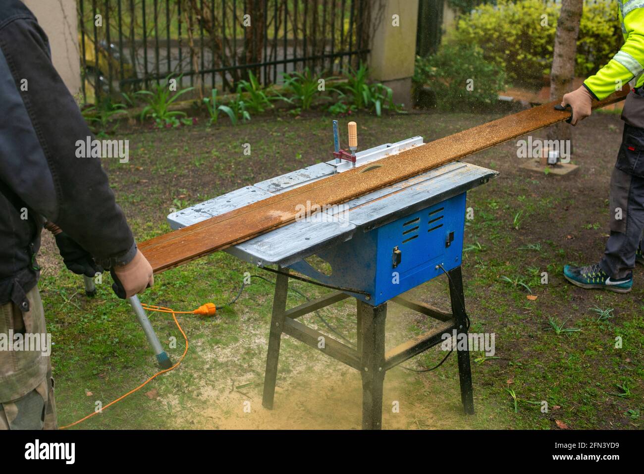 Two men cutting plank for terrace. Construction work in the yard. Stock Photo