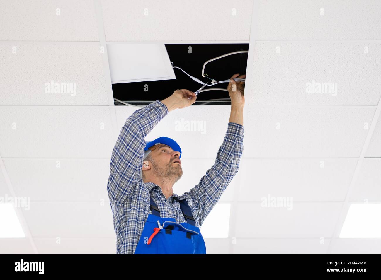Electrician Installing LED Ceiling Light In Office Stock Photo