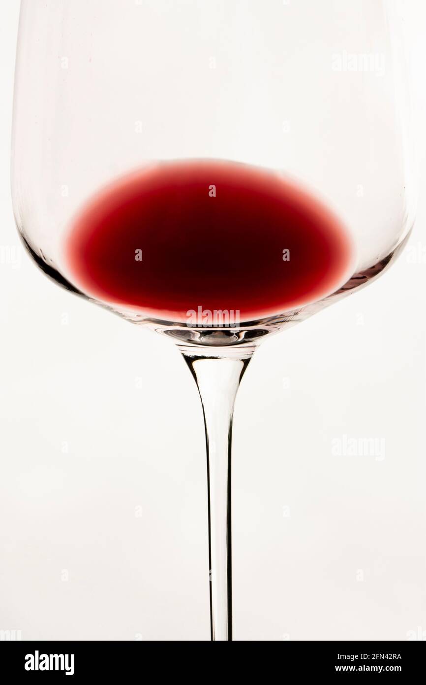 Vertical conceptual close-up photography of an isolated transparent wine glass goblet with a rest of red wine inside, on the white background Stock Photo