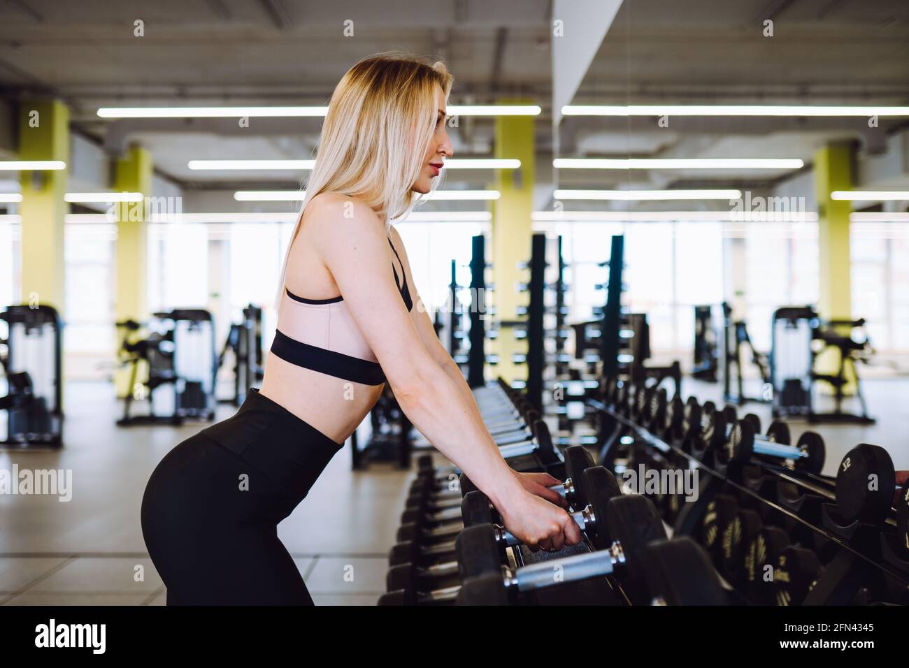 Blonde attractive woman wearing sport bra do exercises with dumbbells ...