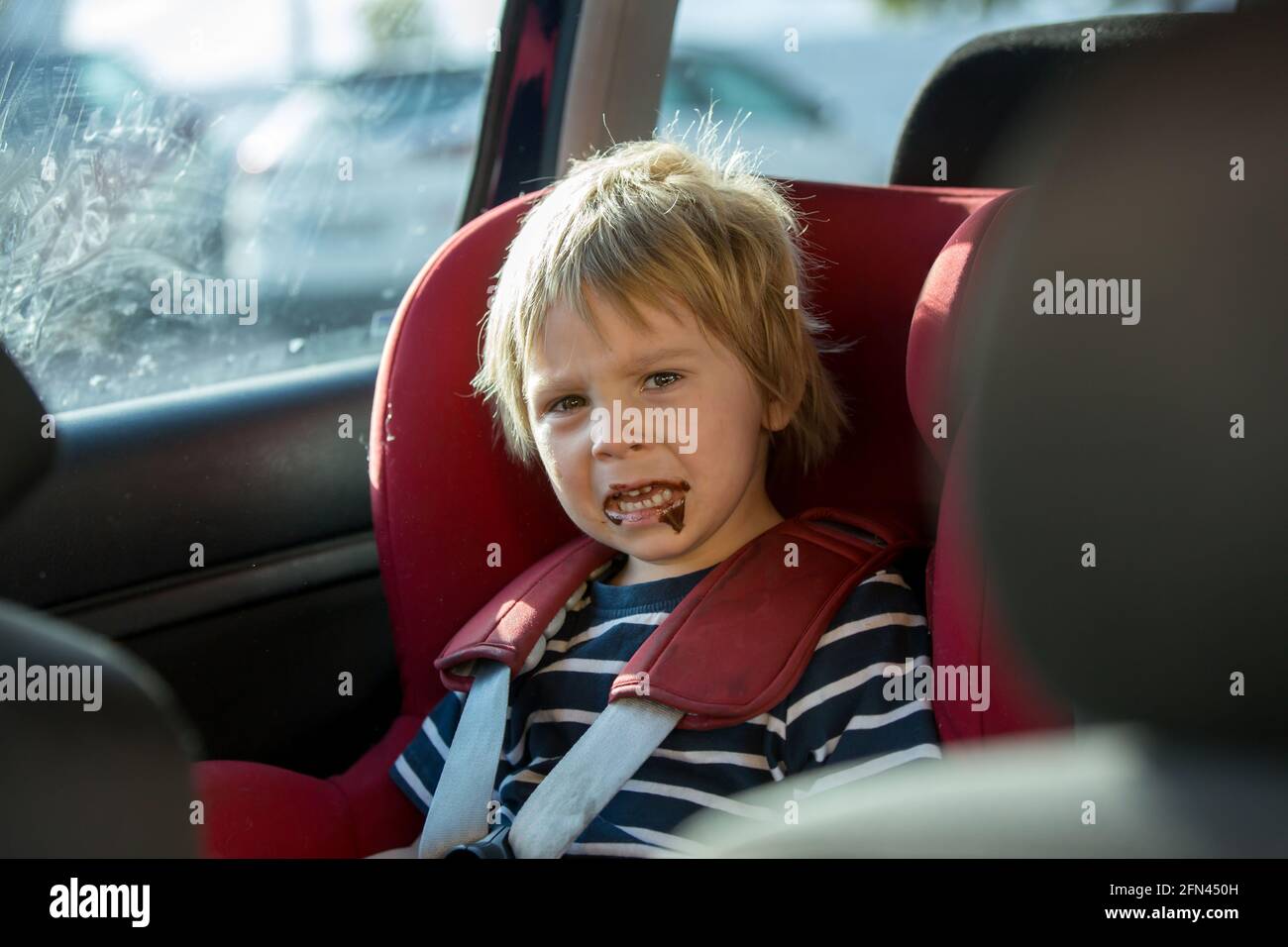 Child, toddler boy, sitting in car seat, eating chocolate, being angry Stock Photo