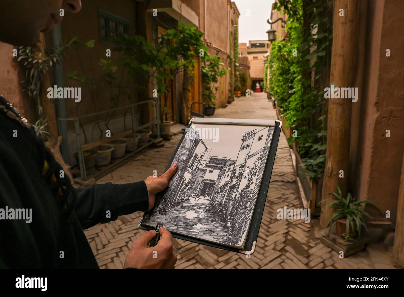 (210514) -- KASHGAR, May 14, 2021 (Xinhua) -- Mamattursunjian Mamatimen paints in an alley in the ancient city of Kashgar in northwest China's Xinjiang Uygur Autonomous Region, May 6, 2021. The dominant color of dwellings in the ancient city of Kashgar in Xinjiang is deep yellow. But in the works of 26-year-old local painter Mamattursunjian Mamatimen, more colors like orange, white, purple, blue. are used to paint the city. That's his feeling of life, and also a feeling shared by the youths in Kashgar, Mamattursunjian said. 'It takes courage to break through the tradition.' Mamattursunjian Stock Photo