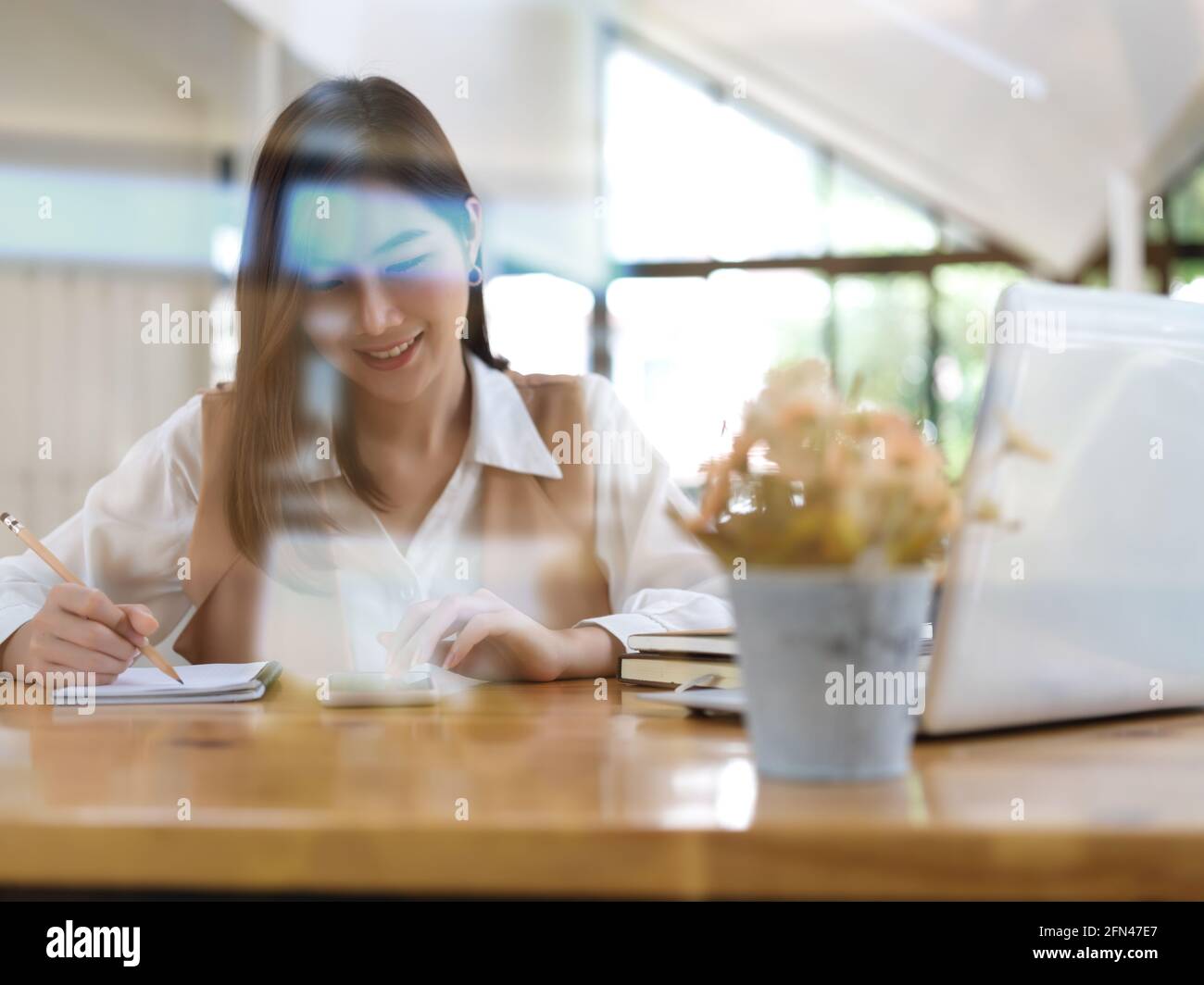 View through glass wall of female student doing homework with ...