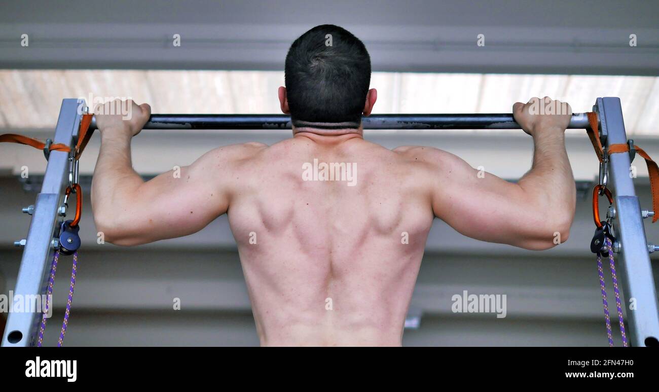 Bodybuilder with massive shoulders and wide back does pull-ups with a bar. Handsome athletic man during workout. Stock Photo