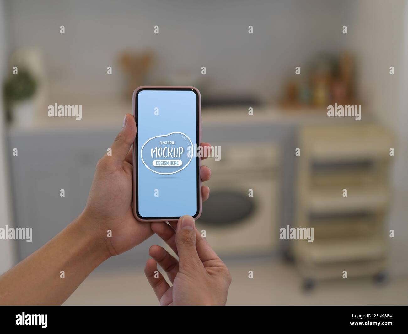 Close up view of hands holding mock up smartphone in blurred kitchen ...