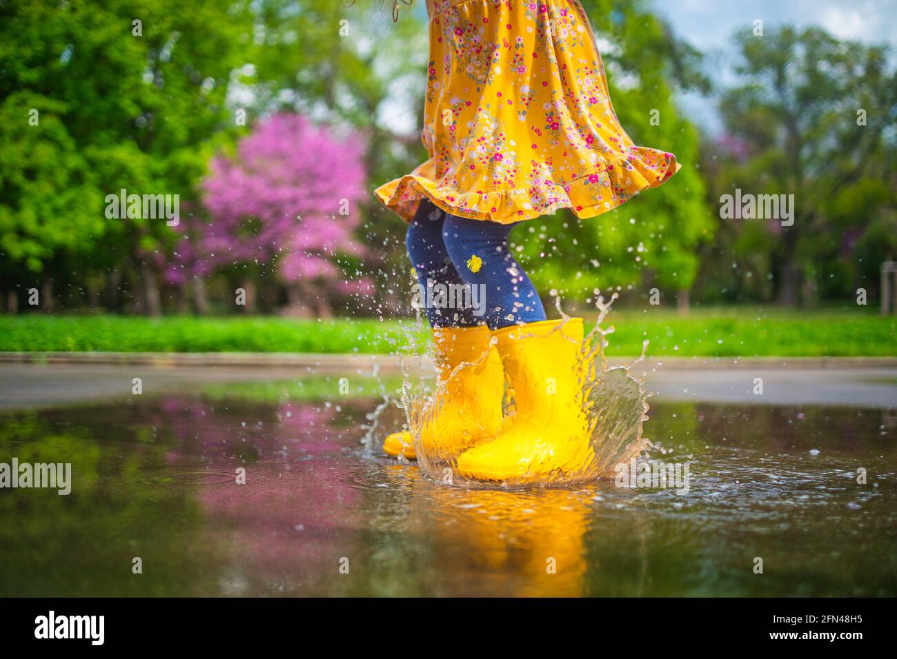 Happy child girl with yellow rubber boots jumping in puddle at the ...