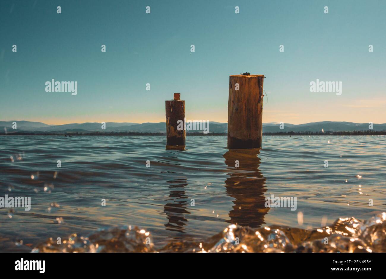 two wooden piles washed by the waters of the lake with the mountains in the background Stock Photo