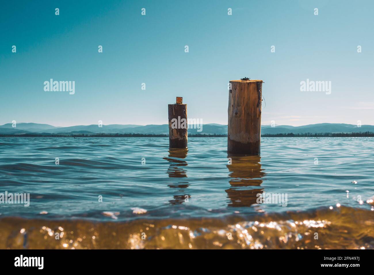 two wooden piles washed by the waters of the lake with the mountains in the background Stock Photo