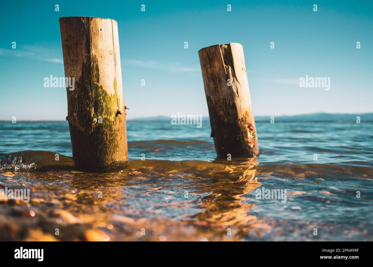 two wooden piles washed by the waters of the lake with the mountains in the background Stock Photo