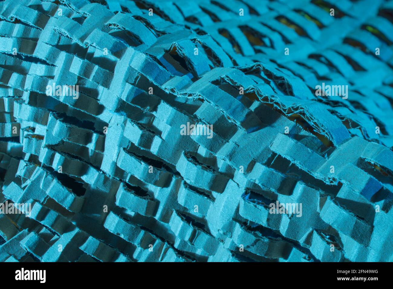 Industrially shredded cardboard packaging in blue light. For recycling