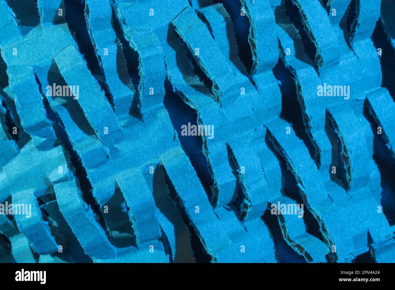 Industrially shredded cardboard packaging in blue light. For recycling waste materials, eco-friendly packaging, abstract shapes, shredding evidence. Stock Photo