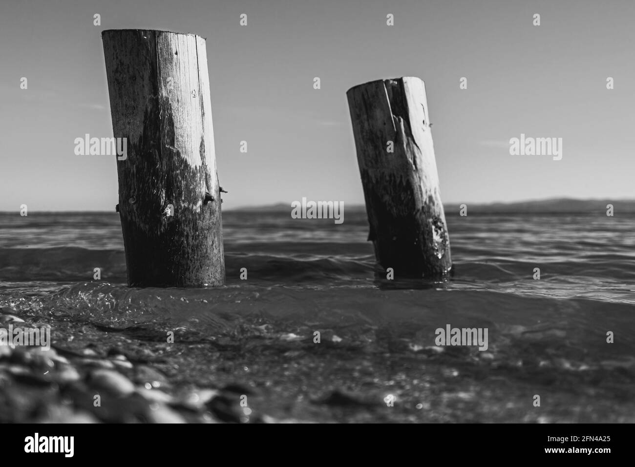 two wooden piles washed by the waters of the lake with the mountains in the background in monochrome Stock Photo