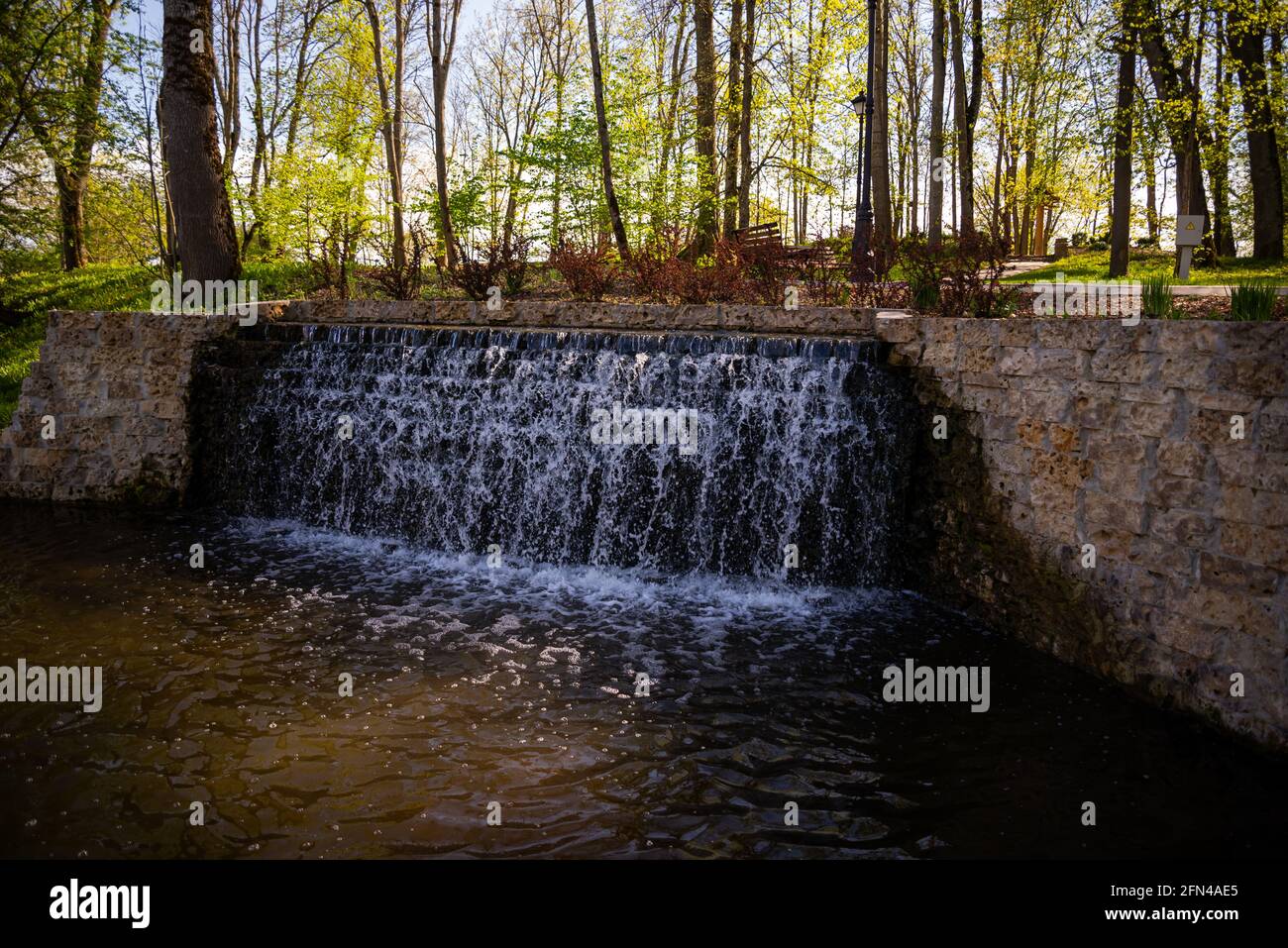 Beautiful waterfall in the park. the waterfall flows from a stone wall structure into a pond. Stock Photo