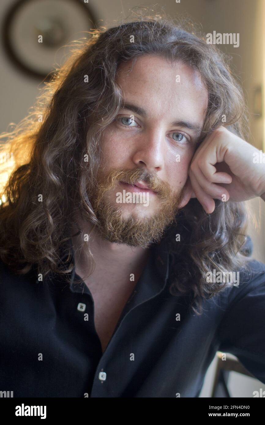 Man with gray eyes, beard and long brown hair. Portrait of young model with serious expression. Metalhead and viking life style. Stock Photo