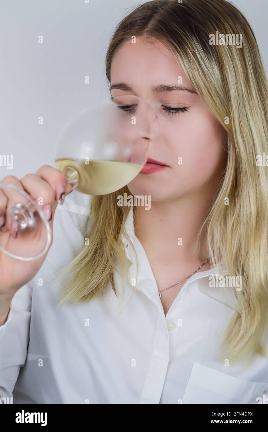 Portrait of a beautiful young blond woman sniffing white wine in the glass to feel its bouquet at a wine tasting Stock Photo