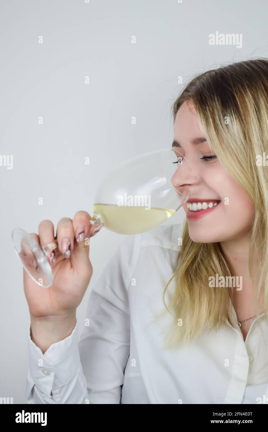 Portrait of a beautiful young blond woman sniffing white wine in the glass to feel its bouquet at a wine tasting Stock Photo
