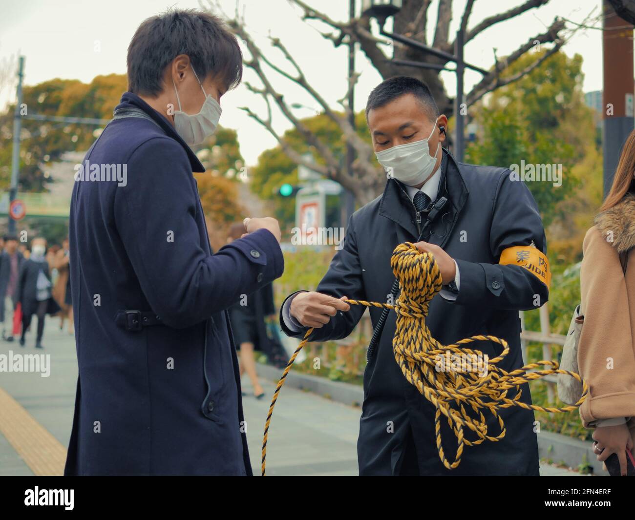 Two Japanese guides arrange a colored rope. Two Asian men with masks organize the route for tourists. Lifestyle and manual skills. Stock Photo