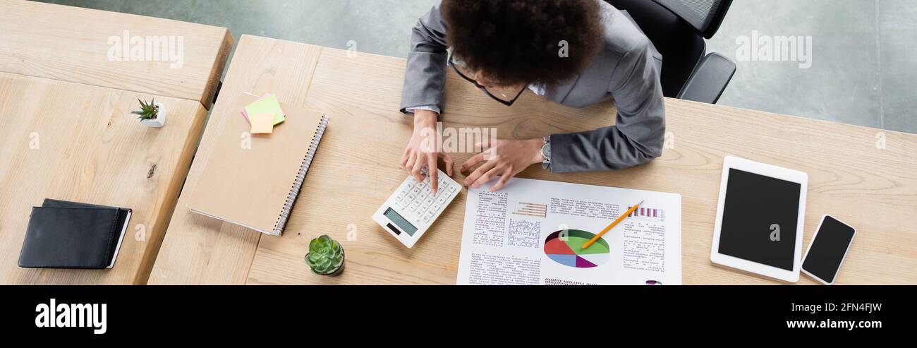 Manager Using Calculator Overhead view of african american manager using calculator near devices ...