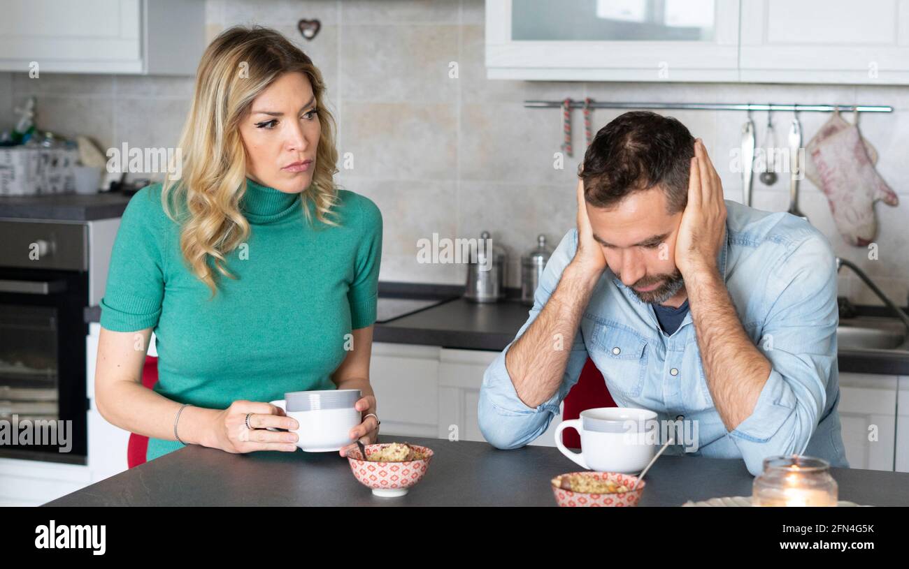 Suspicious woman looks at her worried boyfriend. Dramatic look of a jealous wife scolding frustrated husband during breakfast. Bossy woman. Stock Photo