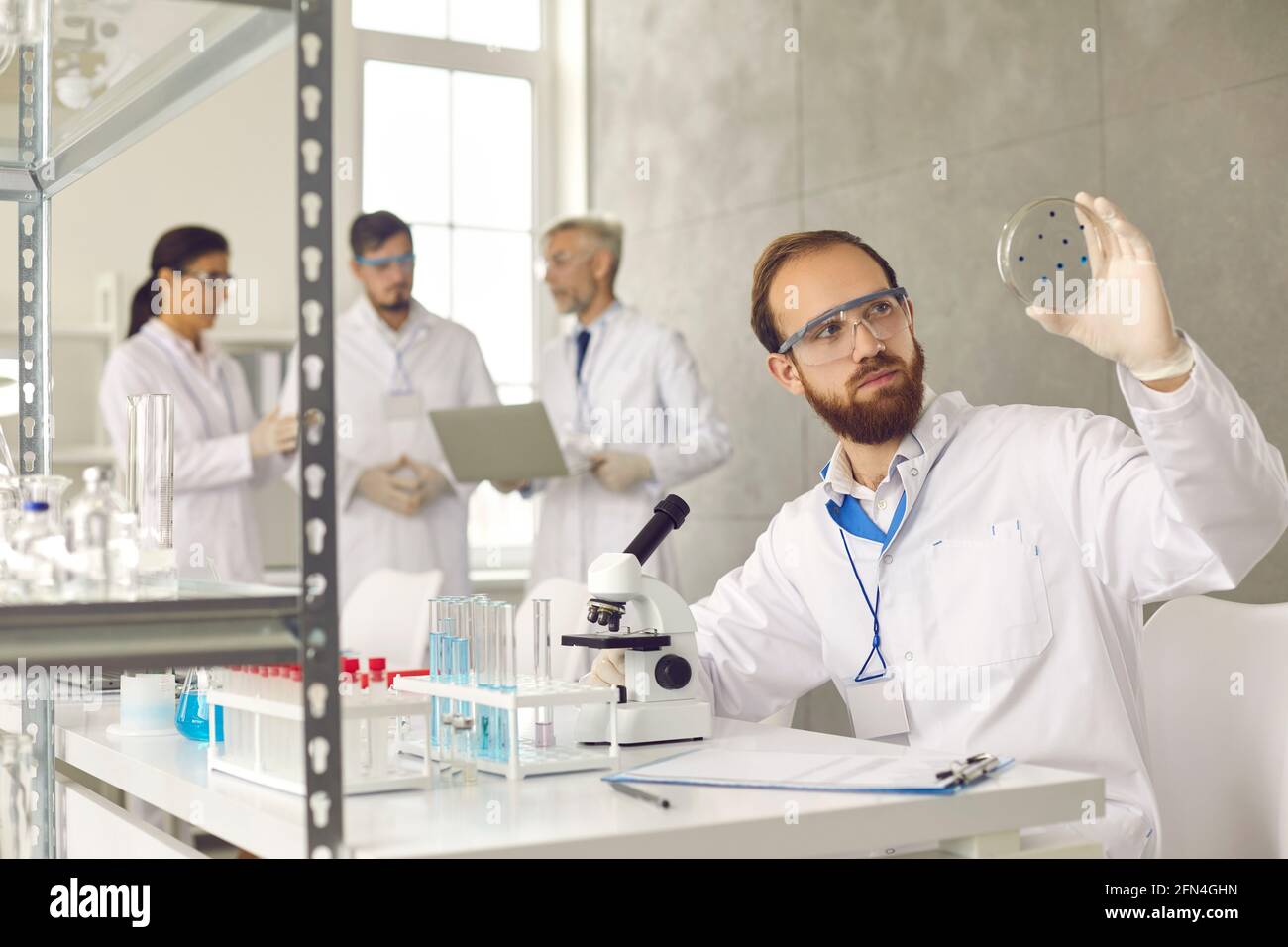 Male scientist analyzing test sample glass slide working at busy laboratory Stock Photo