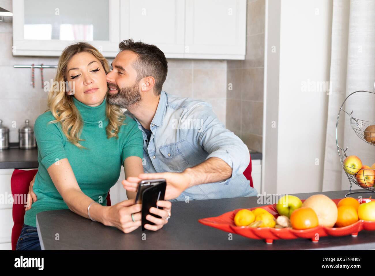 Boyfriend covers his girlfriend's phone camera while kissing her. Funny scene of a newlywed couple. Smartphone addiction and need for attention. Stock Photo