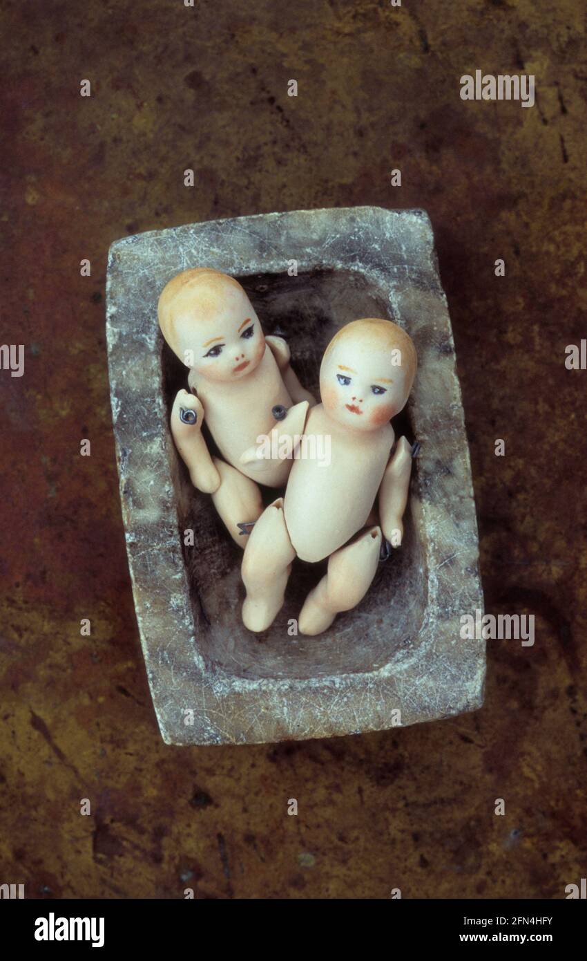 Two small bisque dolls of naked babies with joointed limbs lying in marble dish Stock Photo