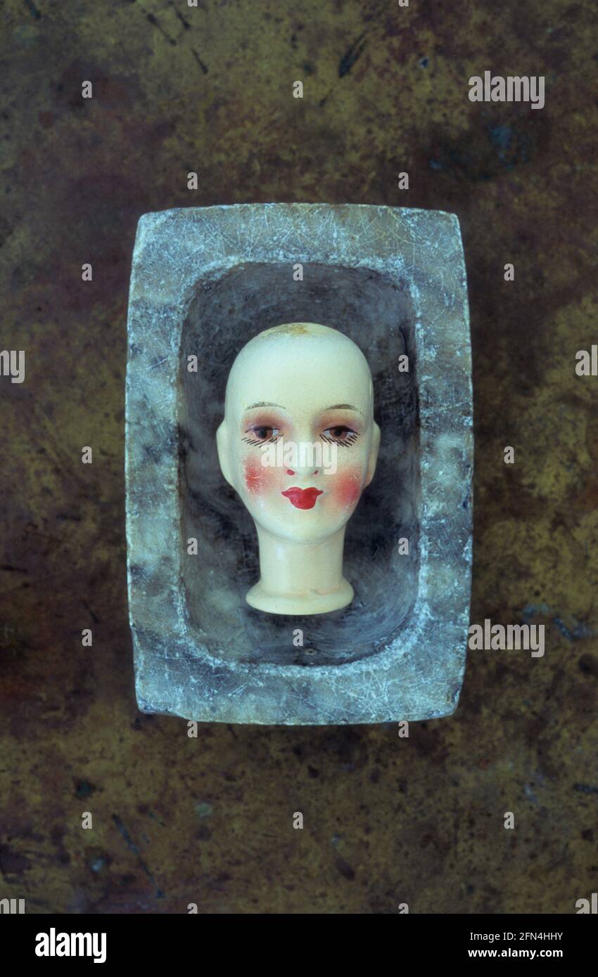 Small bisque head of 1930s adult female doll with exaggerated makeup lying in marble dish Stock Photo