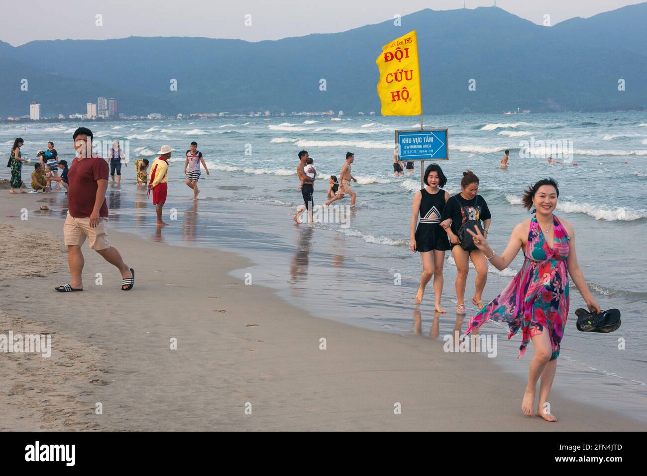 Vietnamese female gives peace sign as she walks barefoot along seashore, My Khe Beach, Da Nang, Vietnam Stock Photo