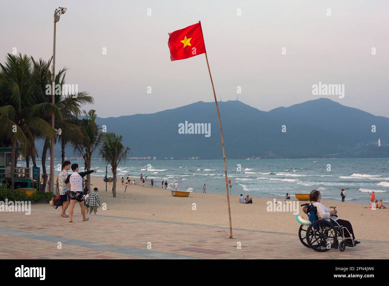 Vietnam flag flying and person in wheelchair observing people on My Khe Beach, Da Nang, Vietnam Stock Photo