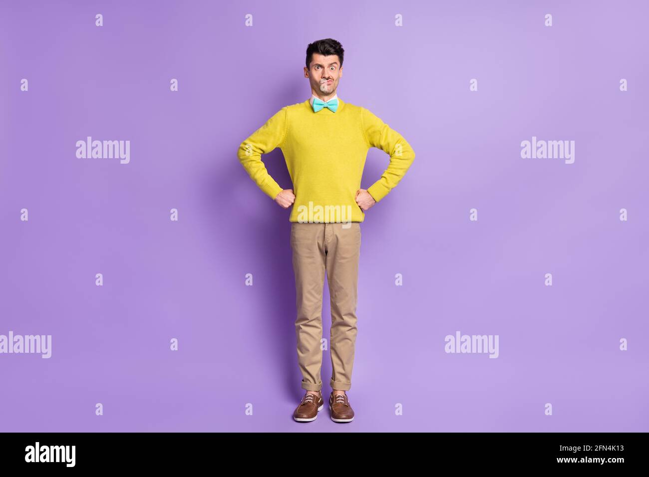 Full size photo of brunet stressed guy stand hands on waist wear yellow sweater trousers sneakers isolated on lilac background Stock Photo
