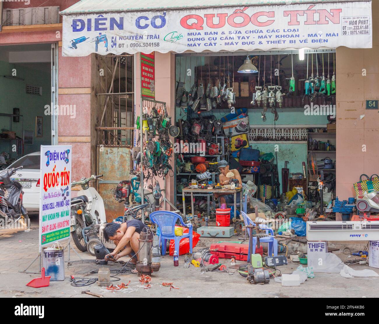 Two Vietnamese engineers working on machinery at their messy pavement workshop, Da Nang, Vietnam Stock Photo