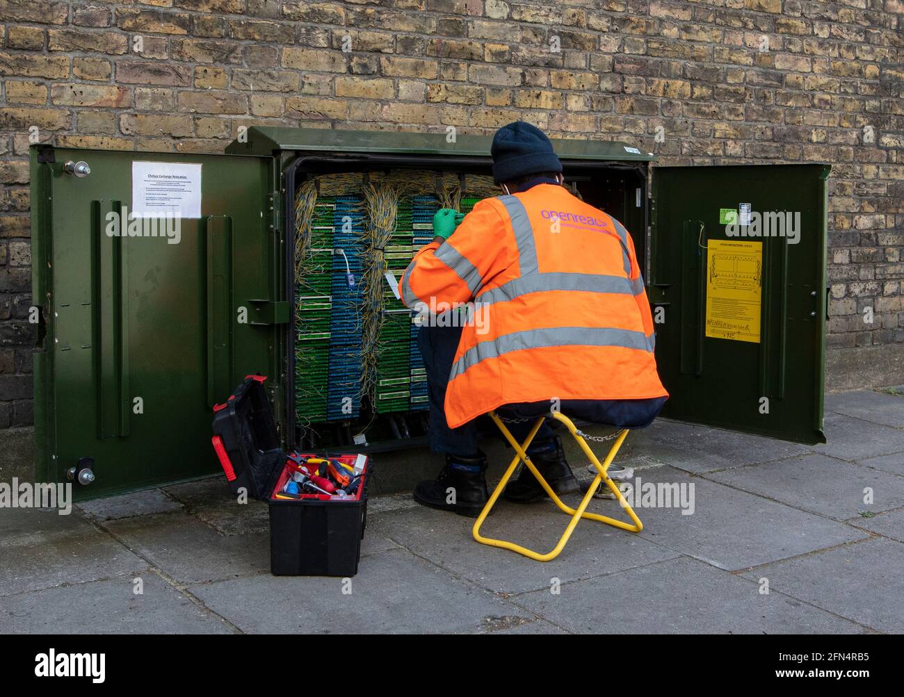 Openreach BT engineer maintaining junction box in central London; he wears a hi-vis jacket and has a yellow stool, with a box of tools. Stock Photo