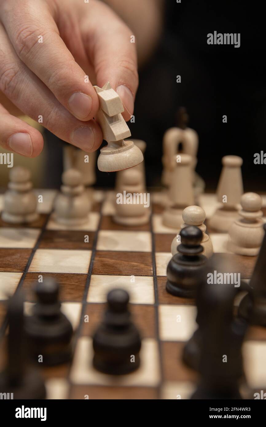 Hand taking next step on chess game. Human hand moving wooden white knight piece Stock Photo