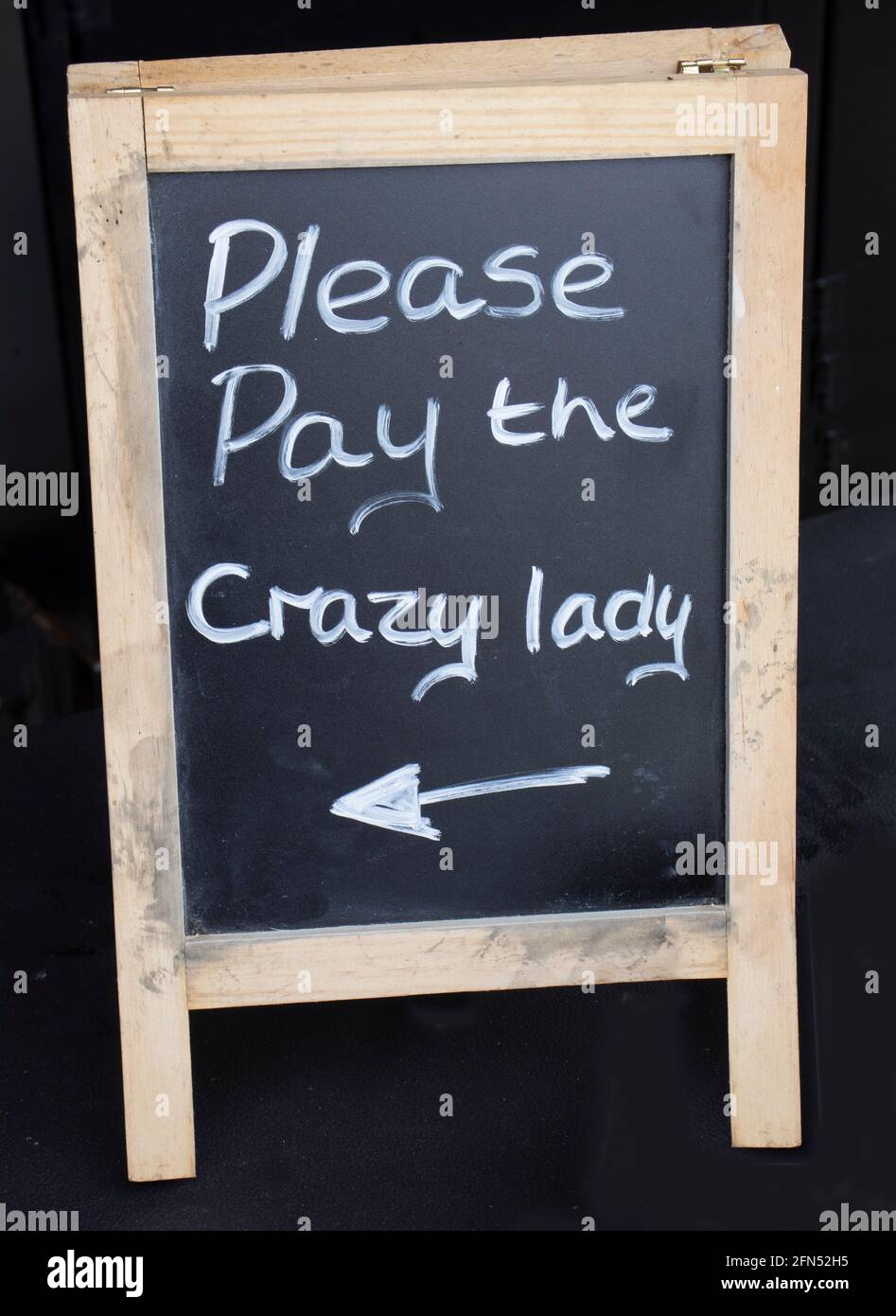 Hand-written blackboard sign at an outdoor food vendor. Stating 'Please Pay The Crazy Lady'. Stock Photo