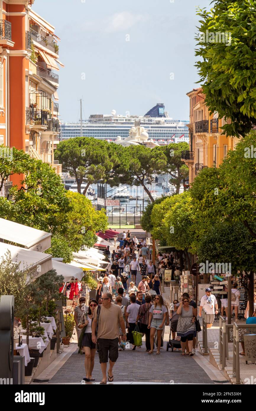 Monaco locals and tourists mingle to eat and shop in a street leading down to the harbour. The Norwegian Pearl cruise ship in the background. Stock Photo