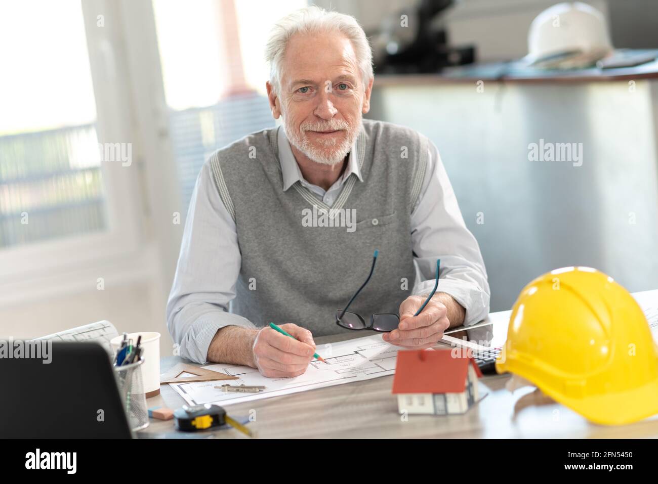 Portrait of senior architect sitting in office and looking at the ...