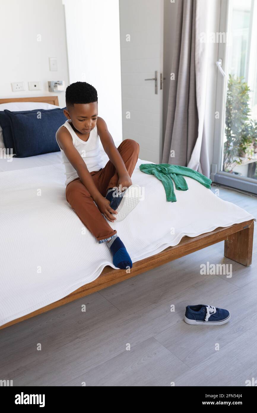 African american boy sitting on bed, putting on shoes Stock Photo Alamy
