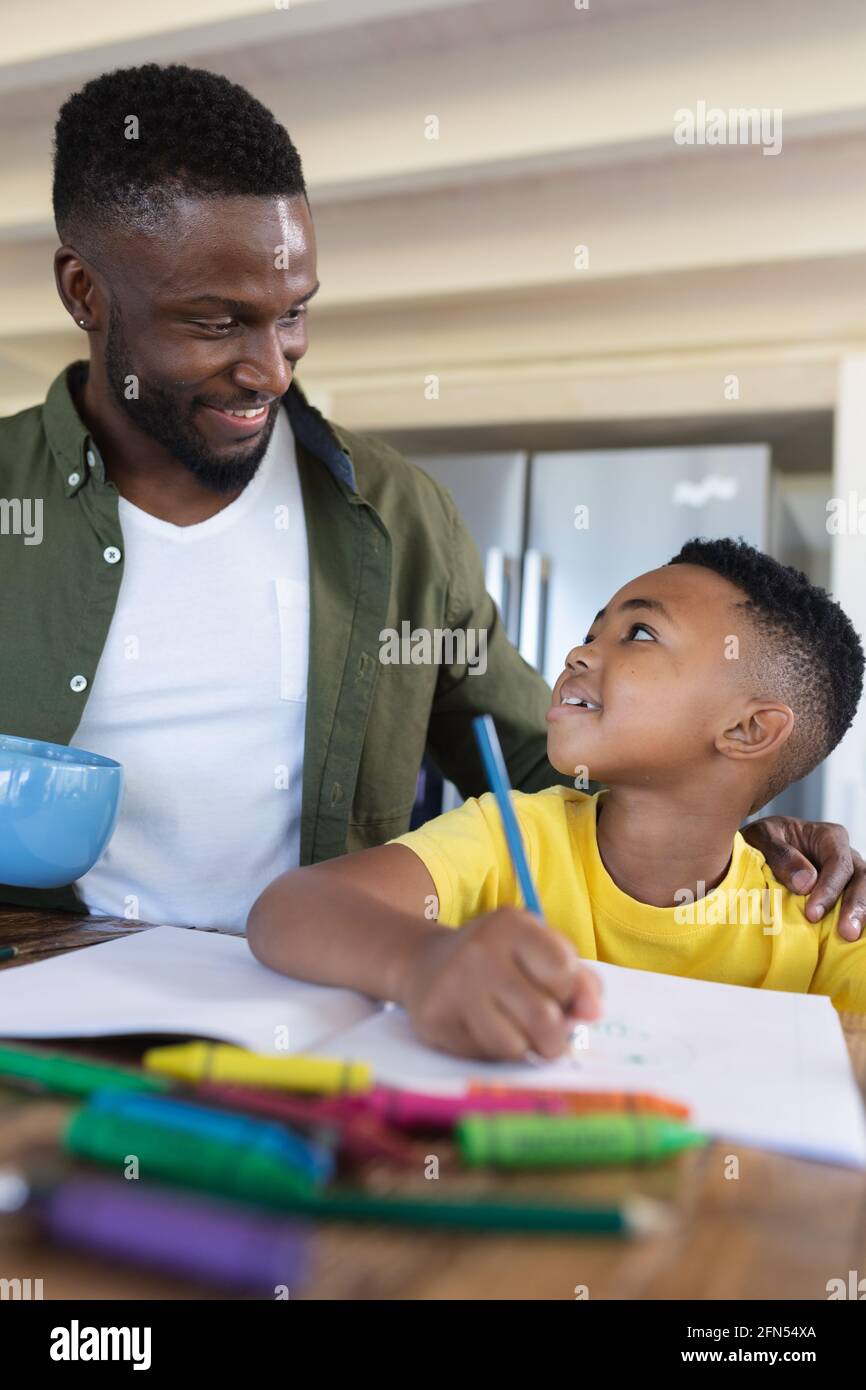 African american father and son sitting at table, writing in notebook smiling Stock Photo