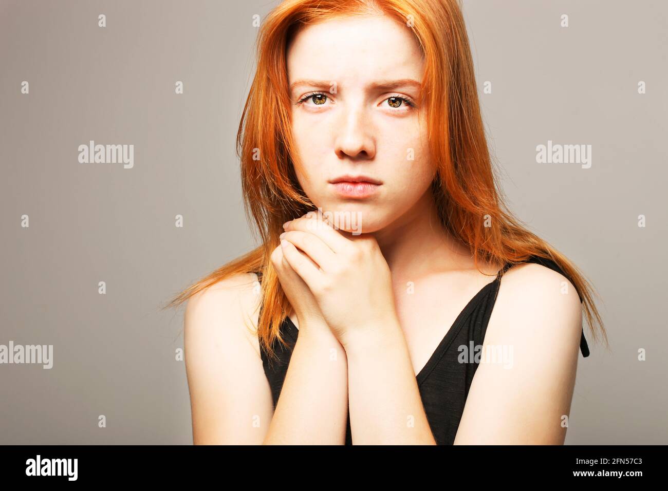 Beautiful fragile redheaded young woman in the dark. Sad frightened girl scared of abuse. Nonverbal behavior, body language. Red hair female looking s Stock Photo