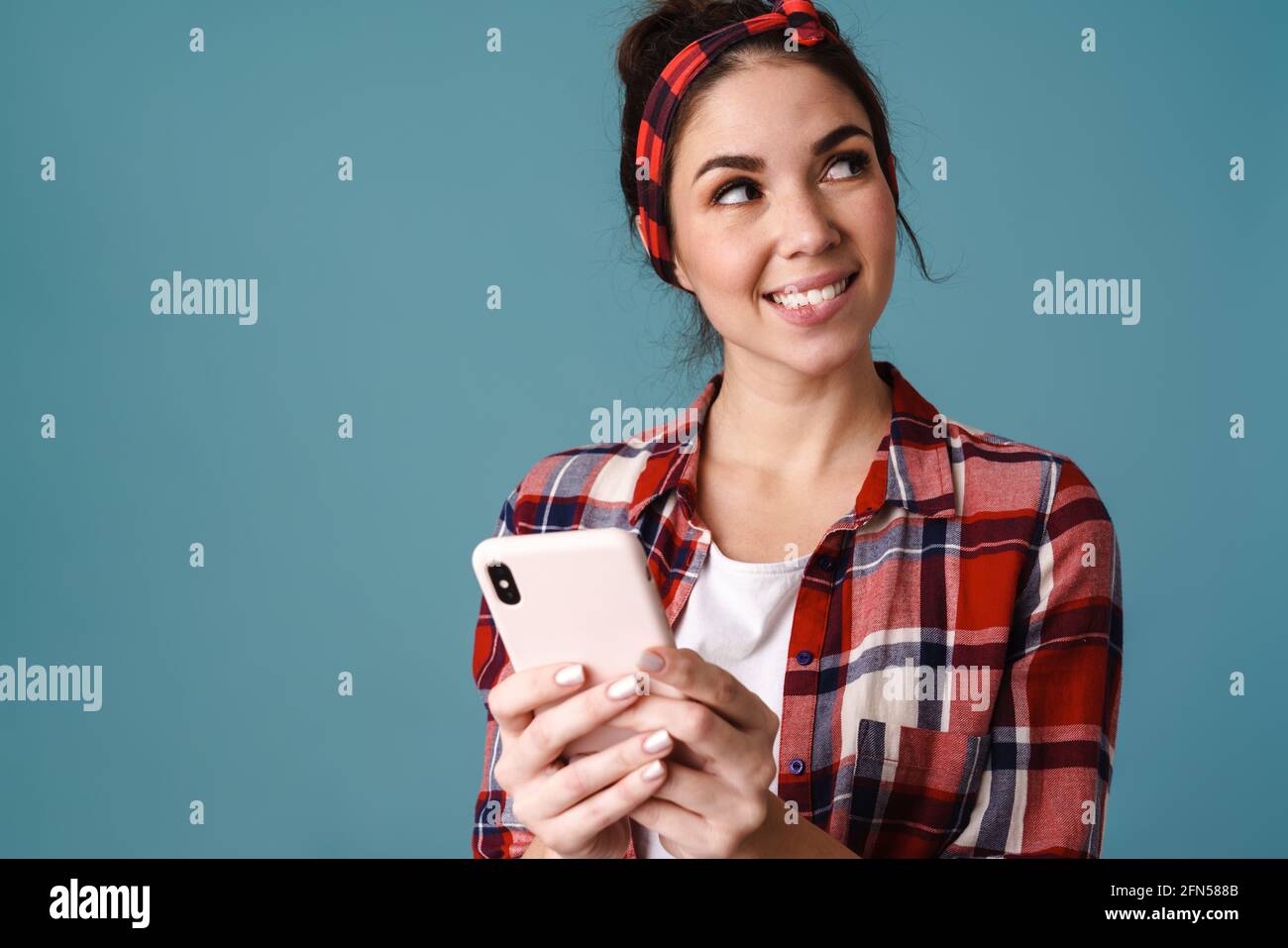 Happy beautiful brunette girl smiling and using mobile phone isolated over blue background Stock Photo