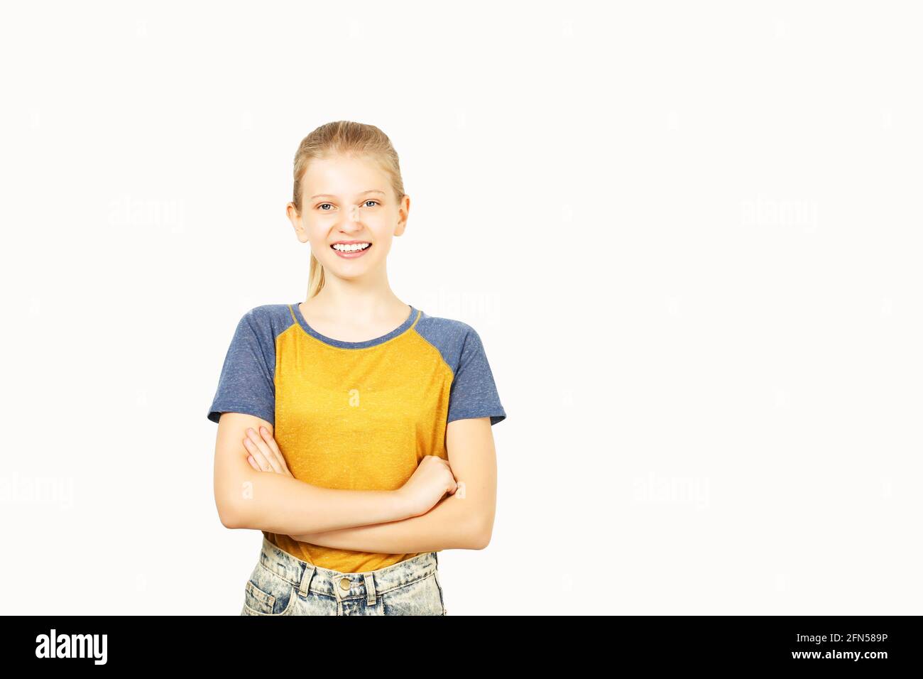 Young beautiful teenage girl with blond hair in ponytail wearing yellow baseball t-shirt with blue sleeves. Pretty female smiling with folded hands st Stock Photo
