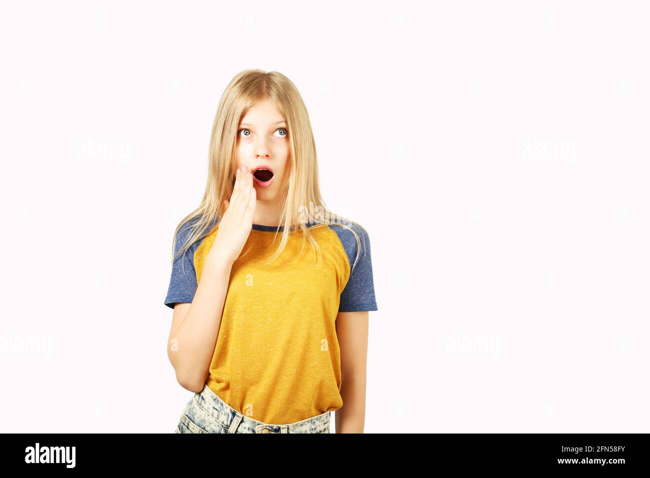 Surprised young teenage girl wearing yellow baseball t-shirt with blue sleeves, shocked facial expression, with mouth wide opened from being astonishe Stock Photo