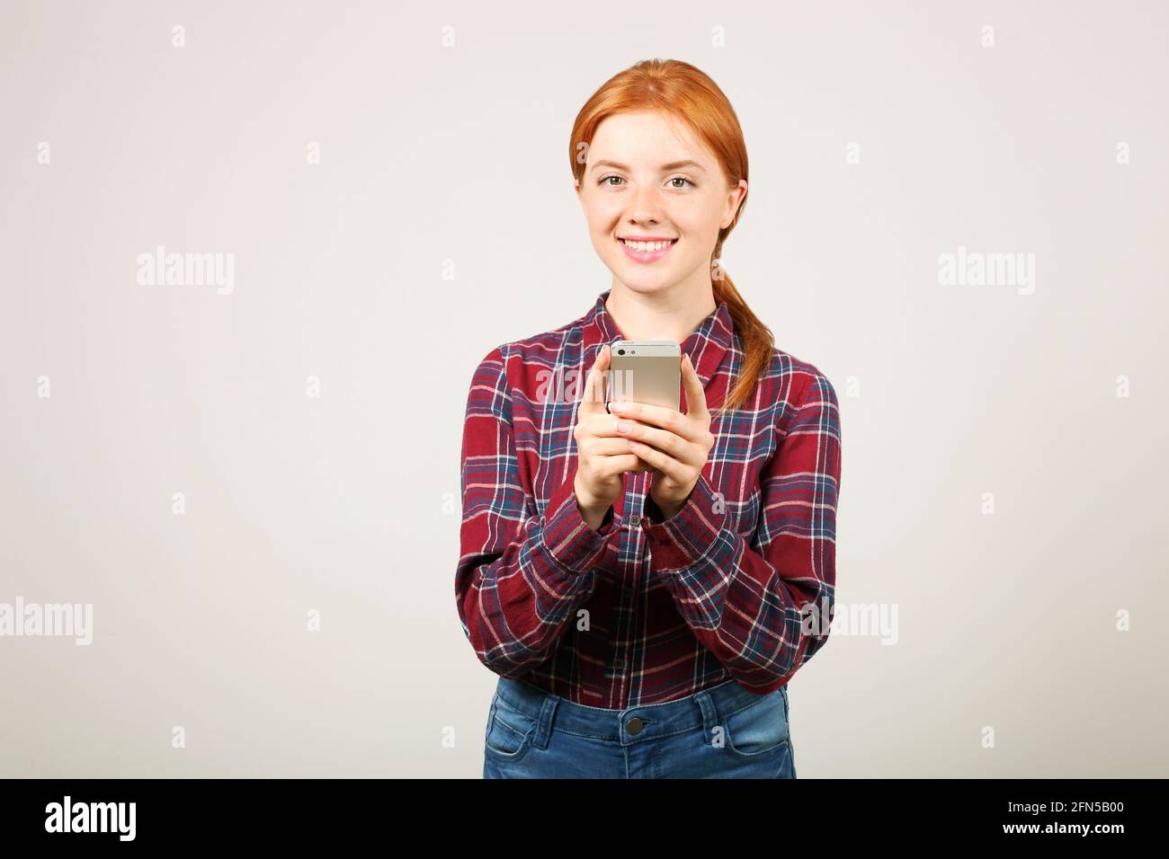 Beautiful young woman wearing flannel shirt holding cell phone looking at  screen & chatting. Female college student using mobile app on smartphone &  s Stock Photo - Alamy