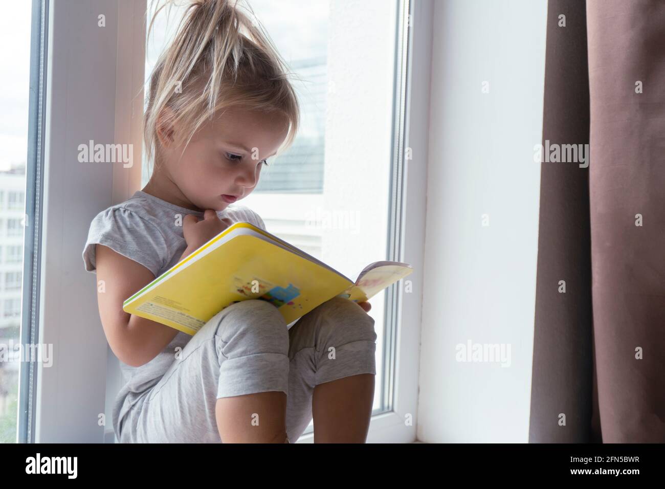 Cute little caucasian child sits near window and reads book Stock Photo ...