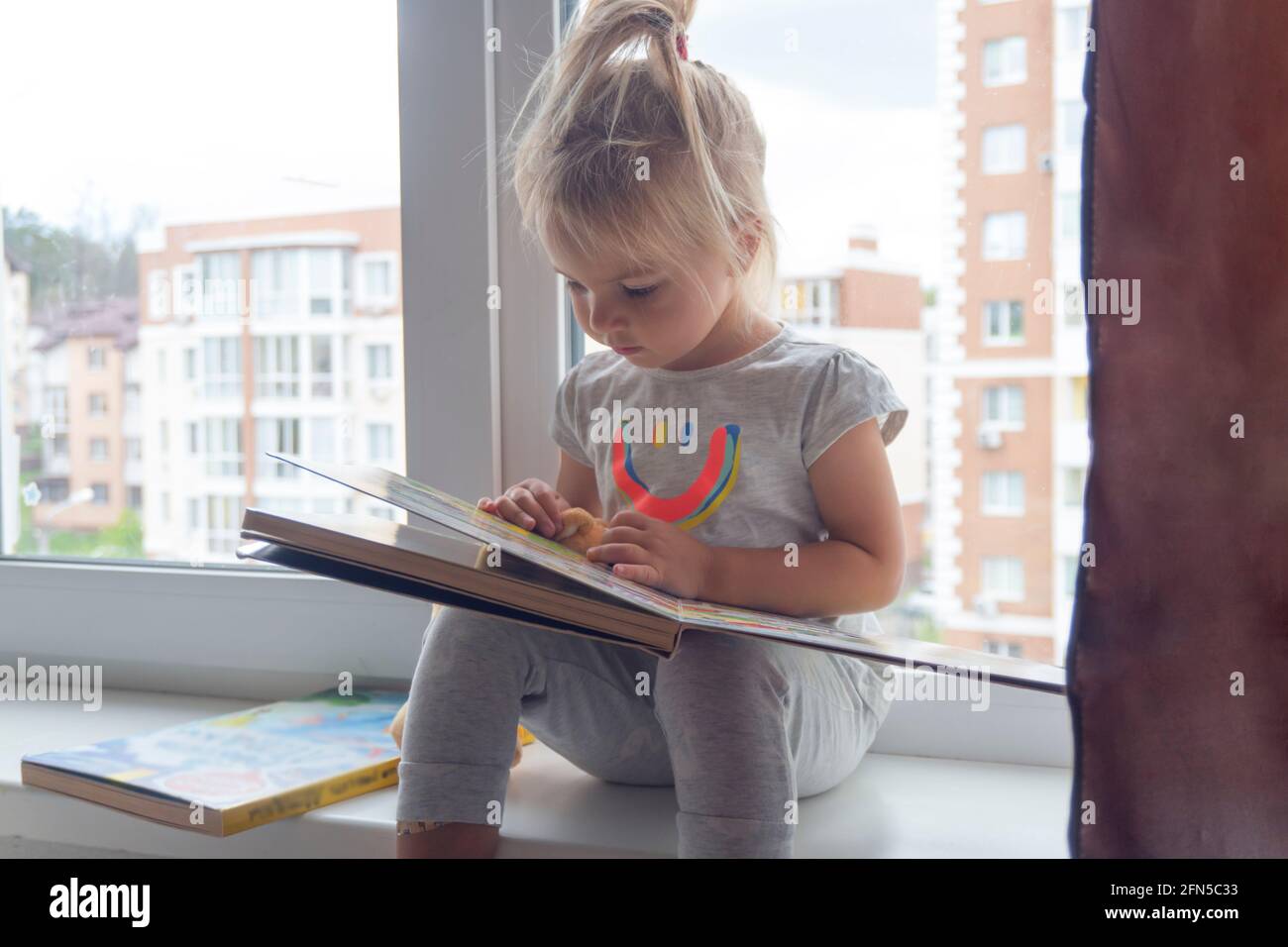 Cute little caucasian child sits near window and reads book Stock Photo ...